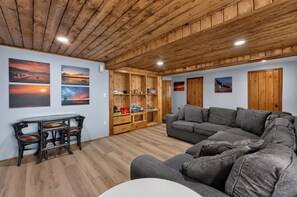A living room with a wooden ceiling, a grey sofa, a wooden cabinet, and a table with chairs.