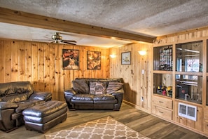 A room with wooden walls, a ceiling fan, a leather sofa, a leather armchair, and a cabinet with memorabilia.