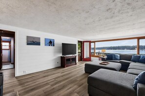 Un salon moderne doté d’un grand téléviseur à écran plat, d’un canapé de couleur foncée et d’un plancher en bois.