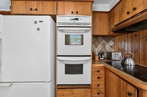 A kitchen with a white refrigerator, a double oven, wooden cabinets, a black countertop, and a kettle. - Diamond Lake Retreat w Private Beach & Dock! (Newport)