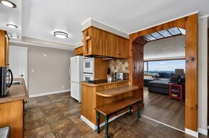 A compact kitchen with built-in appliances, a wooden bench, and a view to a living area.