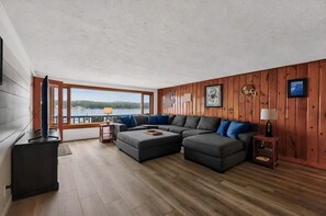 A modern living room with a sectional sofa, a flat-screen TV, and a view of a lake. - Diamond Lake Retreat w Private Beach & Dock! (Newport)