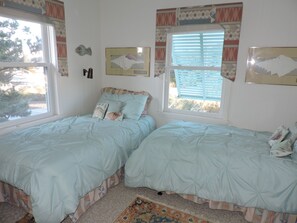 A bedroom with two beds, a patterned rug, and artwork on the walls. - Oceanfront Cozy Retreat | Open Deck & Easy Beach Access | Perfect for Small Fami (Emerald Isle)