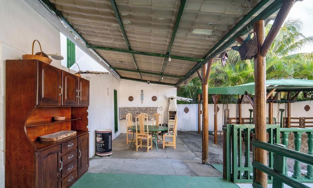 A covered outdoor area with a wooden table and chairs, a cabinet, and a green umbrella.
