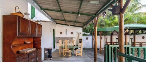 A covered outdoor area with a wooden table and chairs, a cabinet, and a green umbrella.