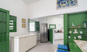 Uma cozinha compacta com geladeira, janela com persianas e parede de tijolos verdes.