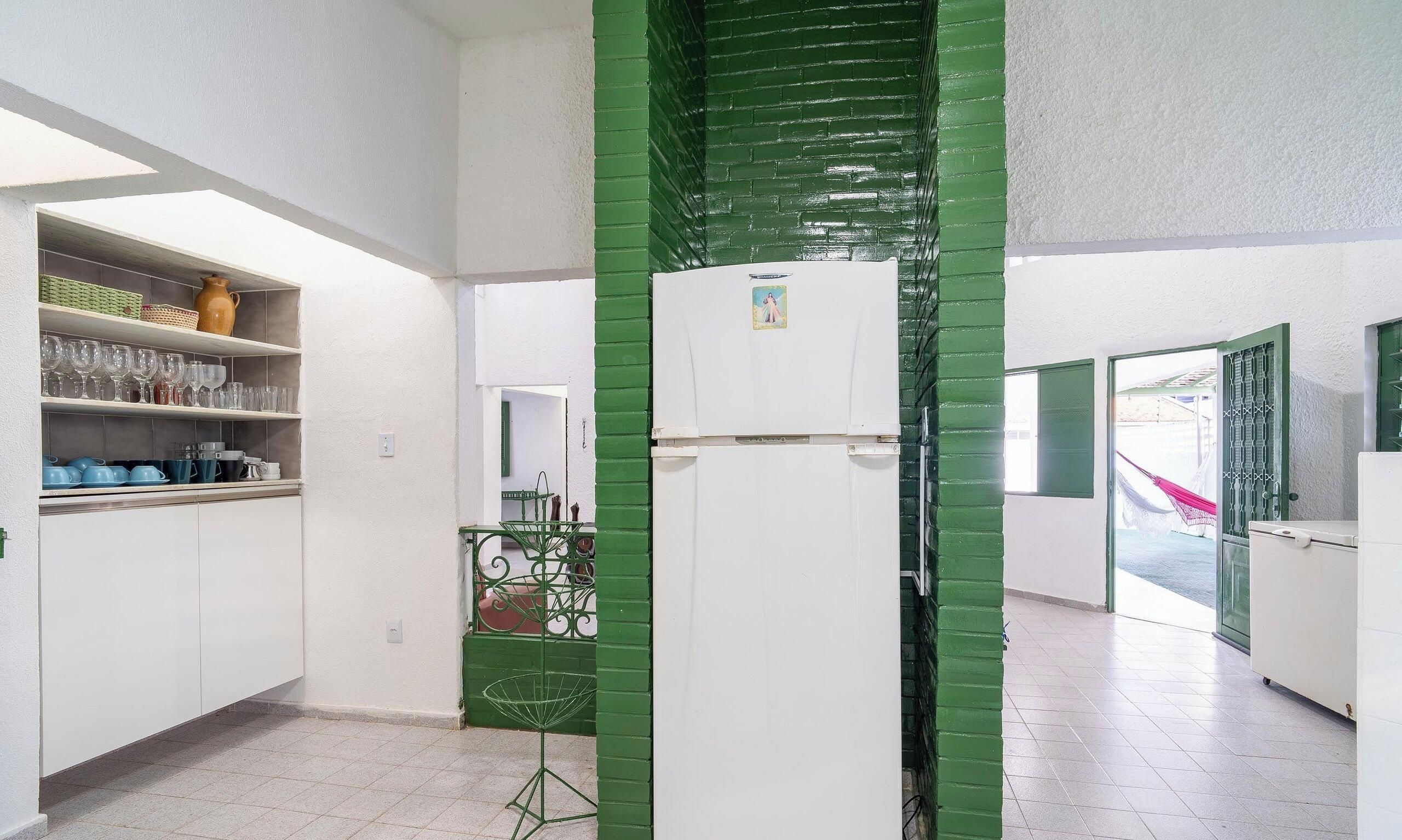 Cozinha com armários brancos, uma parede verde de destaque e uma geladeira.