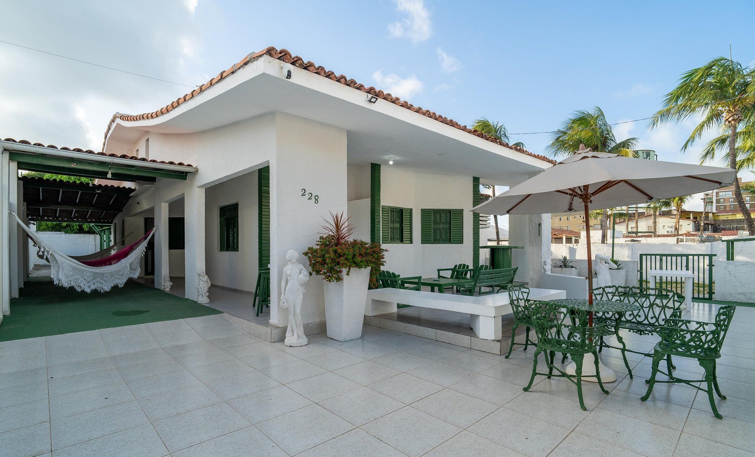 A house with a tiled roof, a hammock, outdoor furniture, and a number '228' on the wall.