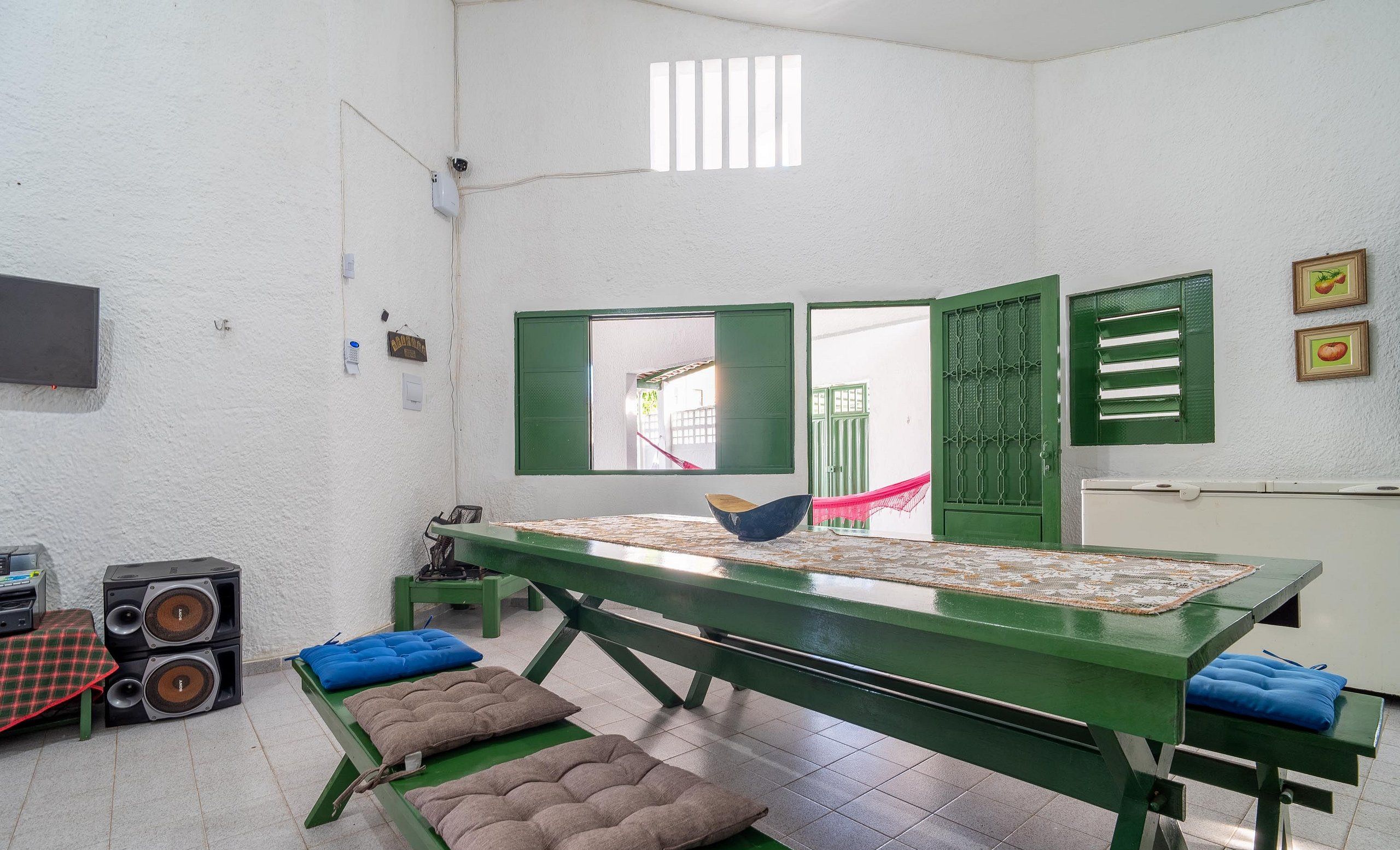 A room with a green table, two speakers, a window with green shutters, and a door with a metal grille.