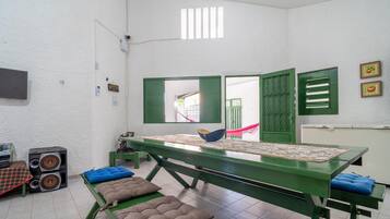 Um quarto com uma mesa verde, dois alto-falantes, uma janela com persianas verdes e uma porta com grades de metal.