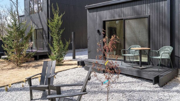 Eine moderne Blockhütte mit einer Terrasse, Sitzgelegenheiten im Freien und einem großen Schiebeglasfenster.