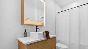 Ein modernes Badezimmer mit einem weißen Waschbecken, einer Holzkommode, einem Spiegel und einer weißen Toilette.