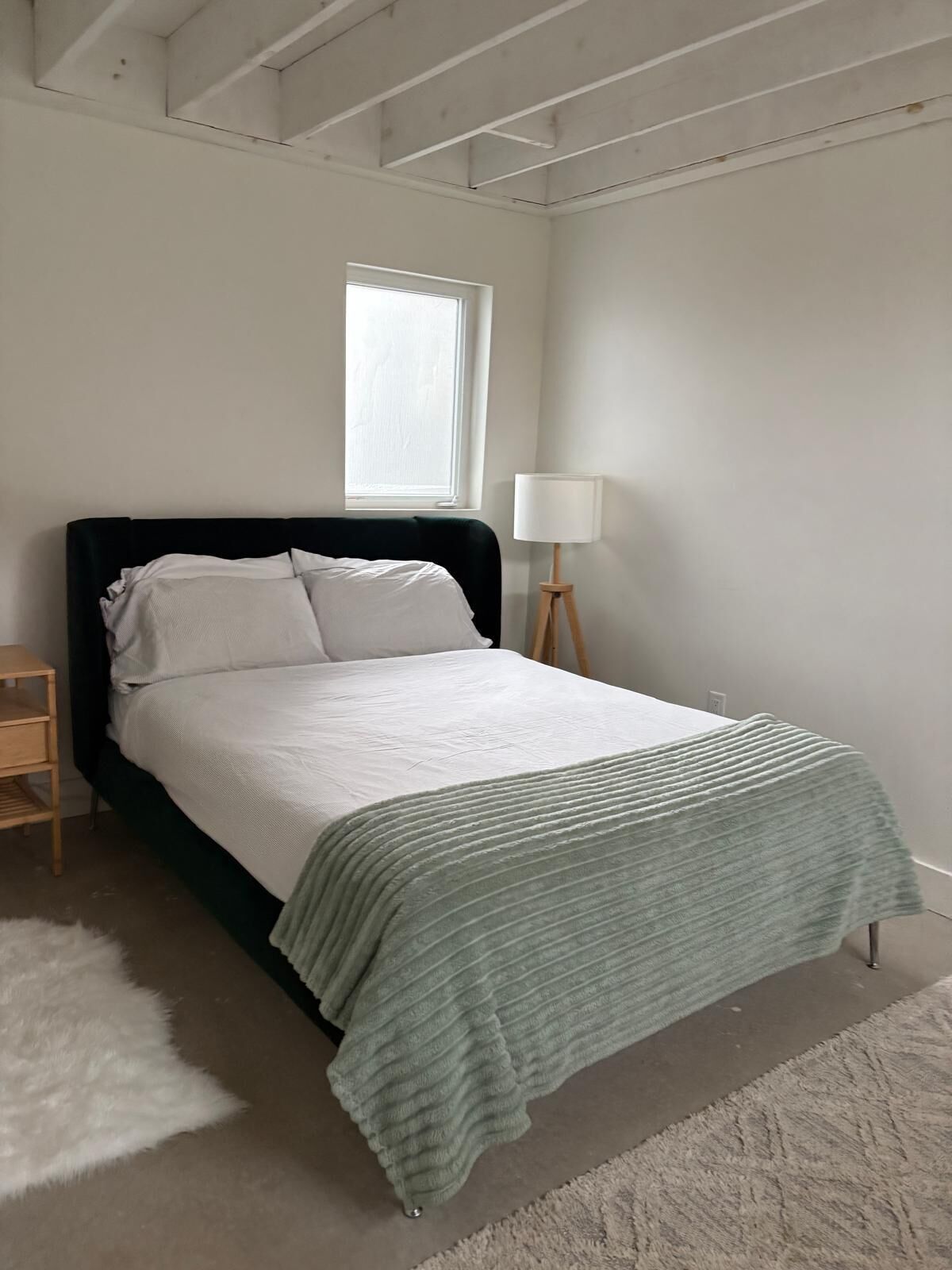 A bed with a dark headboard, a white comforter, and a green throw blanket.