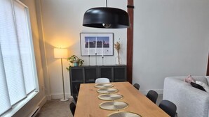 A wooden dining table with white chairs, a black pendant lamp, and a framed picture on the wall.