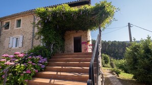 Un bâtiment en pierre avec un escalier menant à une porte, le tout entouré de verdure et de fleurs.