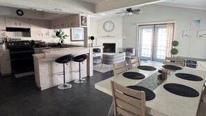 A modern kitchen with a central island, bar stools, a dining table with black mats, and a fireplace. - Sun, Pool & Beach: Largo Getaway (Largo)