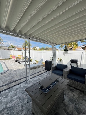 Ein überdachter Patio-Bereich mit Gartenmöbeln, einem Grill und einem Pool.