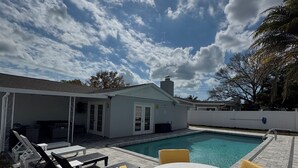 A poolside area with a white table and chairs, a covered seating area, and a view of the sky. - Sun, Pool & Beach: Largo Getaway (Largo)