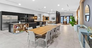 A modern kitchen with a central island, a dining area with a wooden table and chairs, and a large window providing natural light. - Star Villa Opulent Waterfront Property (North Miami Beach)