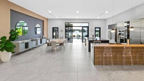 A modern kitchen with a central island, a dining area with a table and chairs, and a large window providing a view of the outdoors.