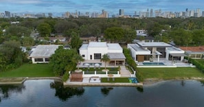 A modern house with a swimming pool, surrounded by greenery and a city skyline in the background. - Star Villa Opulent Waterfront Property (North Miami Beach)