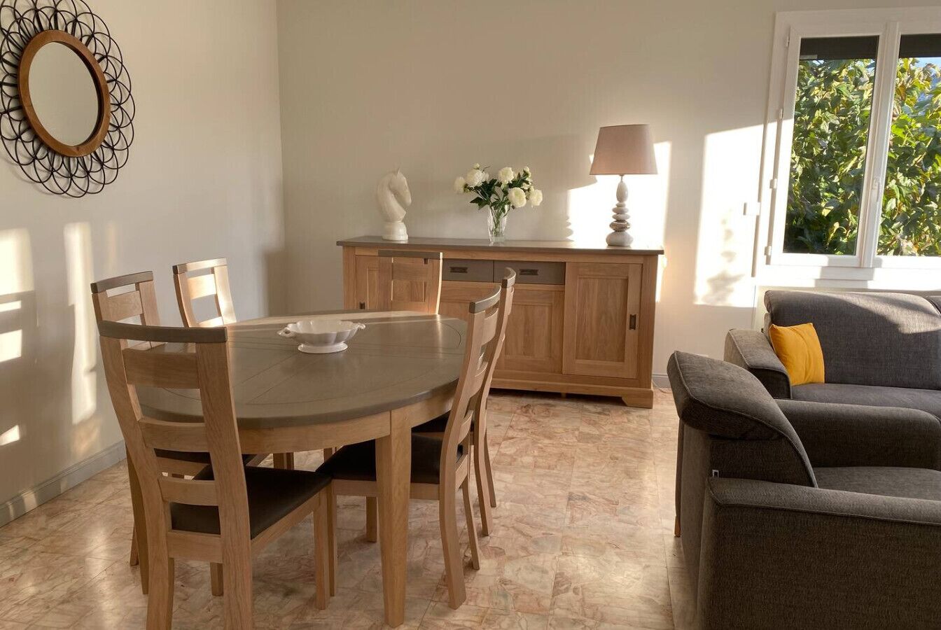 A dining area with a round table and chairs, a wooden cabinet, a lamp, and a sofa with a cushion.