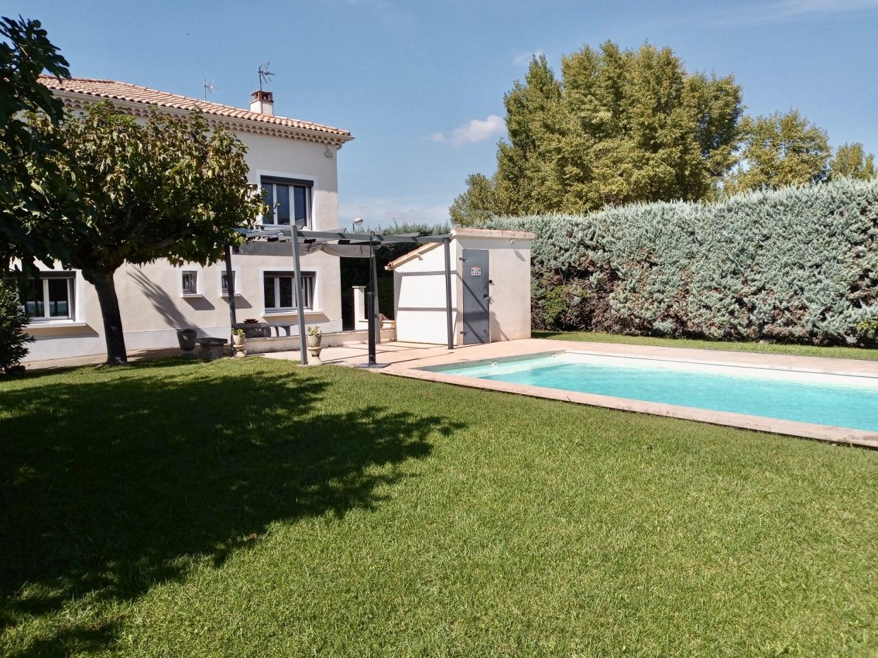 A residential property with a swimming pool, a covered patio, and a well-maintained lawn.