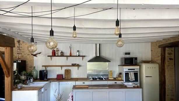 Une cuisine dotée d’un îlot central en bois, de meubles blancs, d’une hotte en acier inoxydable et d’un réfrigérateur au style rétro.