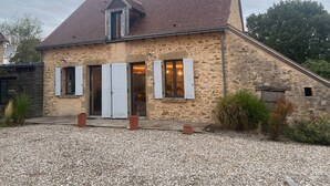 Une maison en pierre avec un toit en pente, une porte d’entrée et des fenêtres dotées de volets.