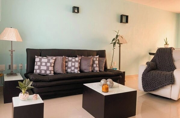 A modern living room with a black sofa, two side tables, a white armchair, and a floor lamp.