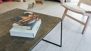 Un salon avec une table basse, des livres, un meuble rose et un tableau.