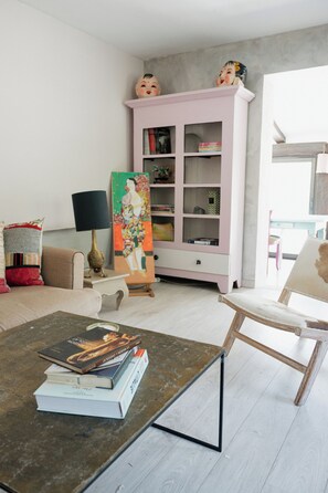 A living room with a coffee table, books, a pink cabinet, and a painting. - Charming house 5mn away from Valbonne, in a residence with pool and tennis (Opio)