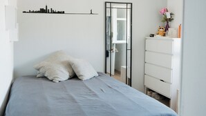 Une chambre à coucher comprenant un lit, une commode, un miroir et une décoration murale représentant un paysage urbain.