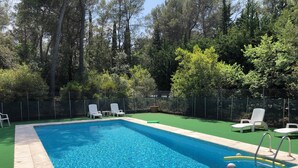 Une piscine rectangulaire à l’eau d’un bleu limpide, entourée d’une pelouse verdoyante et d’une clôture en treillis métallique.