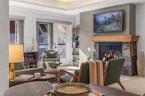 Una sala de estar acogedora con chimenea, un televisor montado encima y una estantería llena de libros y objetos decorativos.