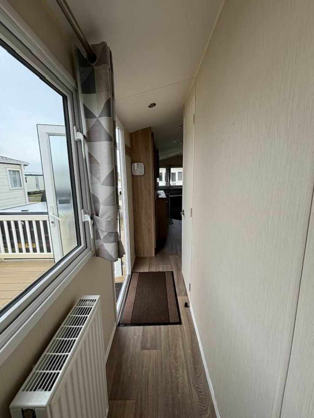 A narrow hallway with a window on the left, a door at the end, and a view of a deck outside. - cosy camber home from home caravan (Camber)