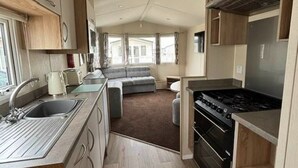 A compact RV kitchen with a stove, sink, and a small dining area. - cosy camber home from home caravan (Camber)