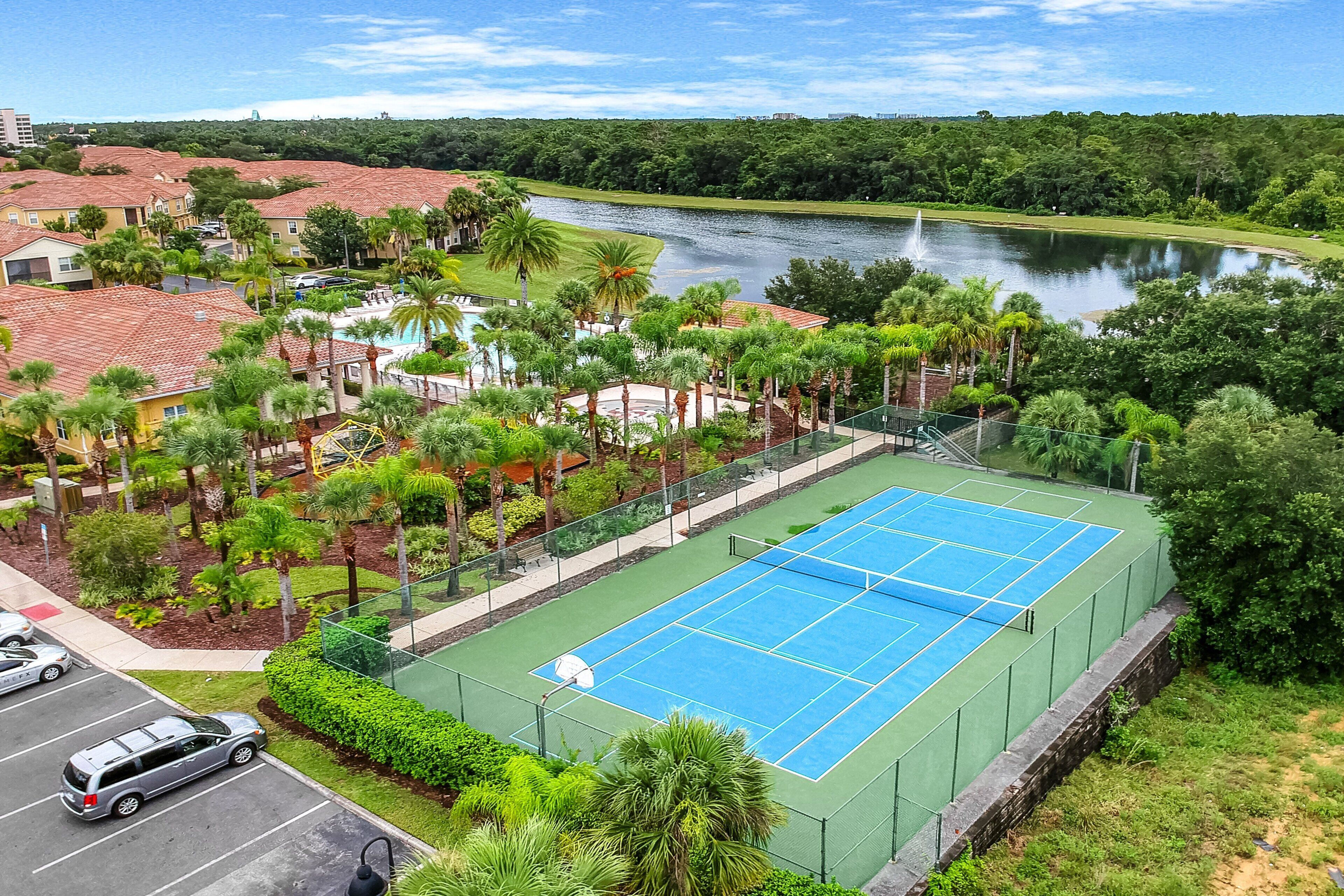 A tennis court surrounded by greenery and a body of water.