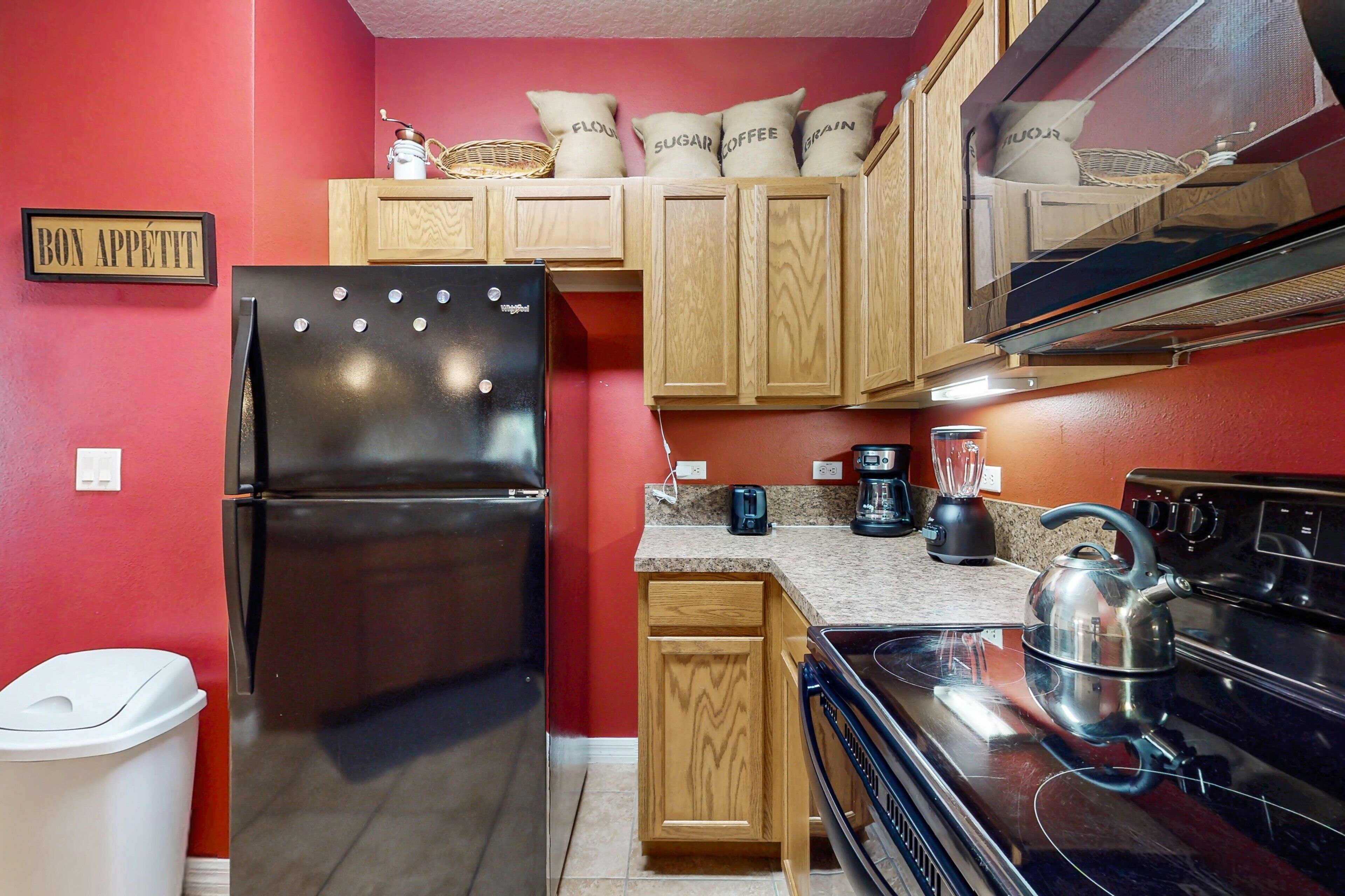 Una cocina con un refrigerador negro, armarios de madera, una estufa y un hervidor.
