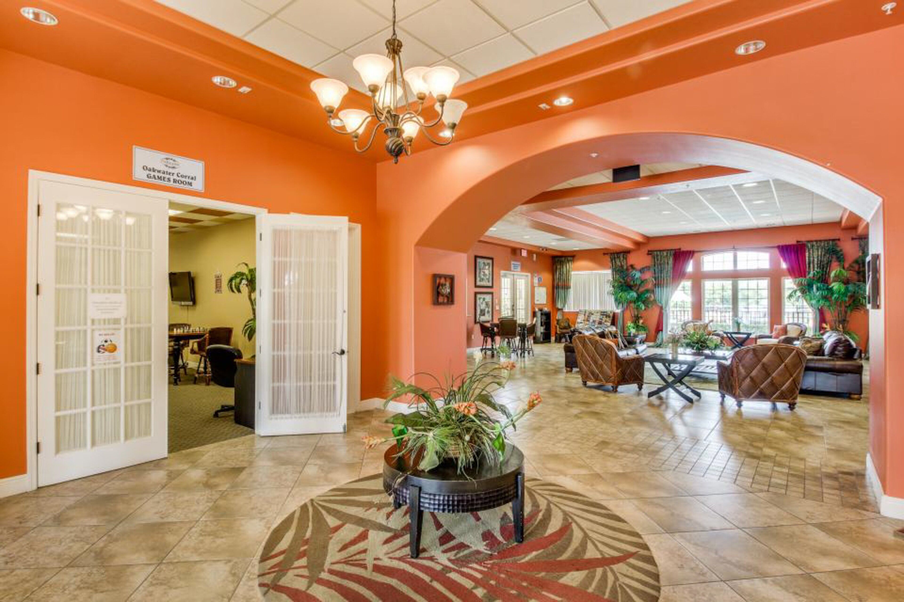 A hotel lobby with an orange color scheme, a chandelier, a games room sign, and a reception desk.