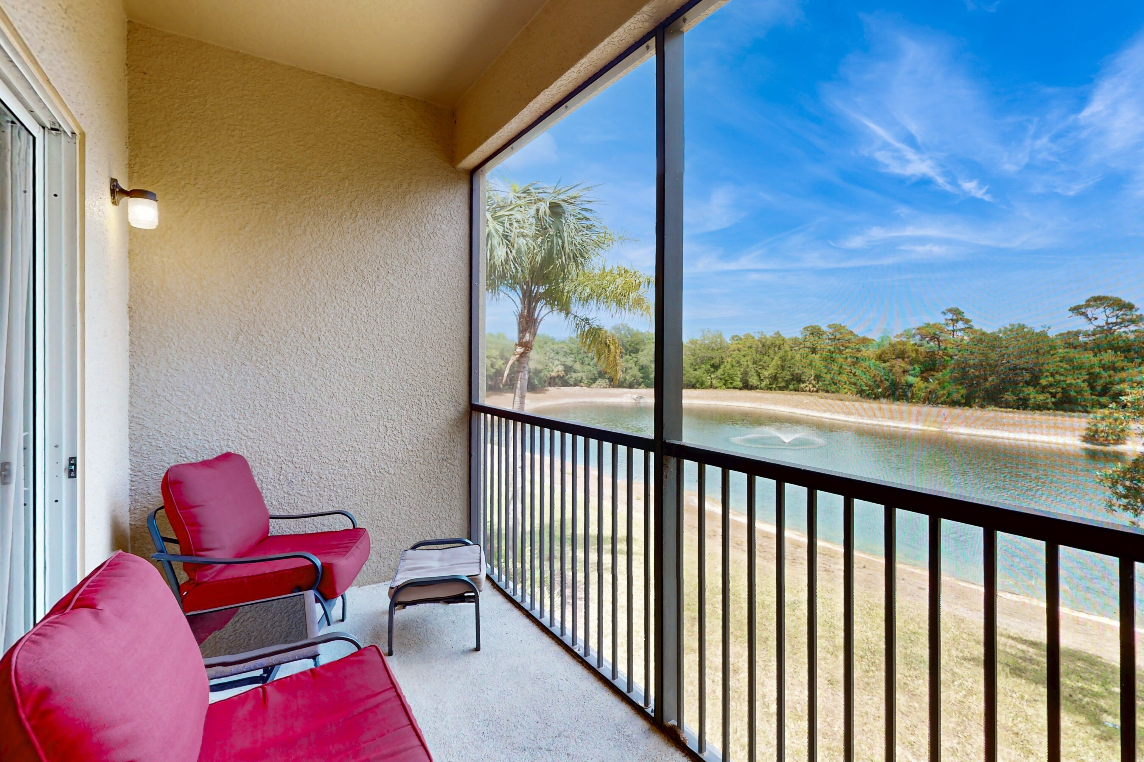 A balcony with red chairs, a small table, and a view of a body of water and greenery.