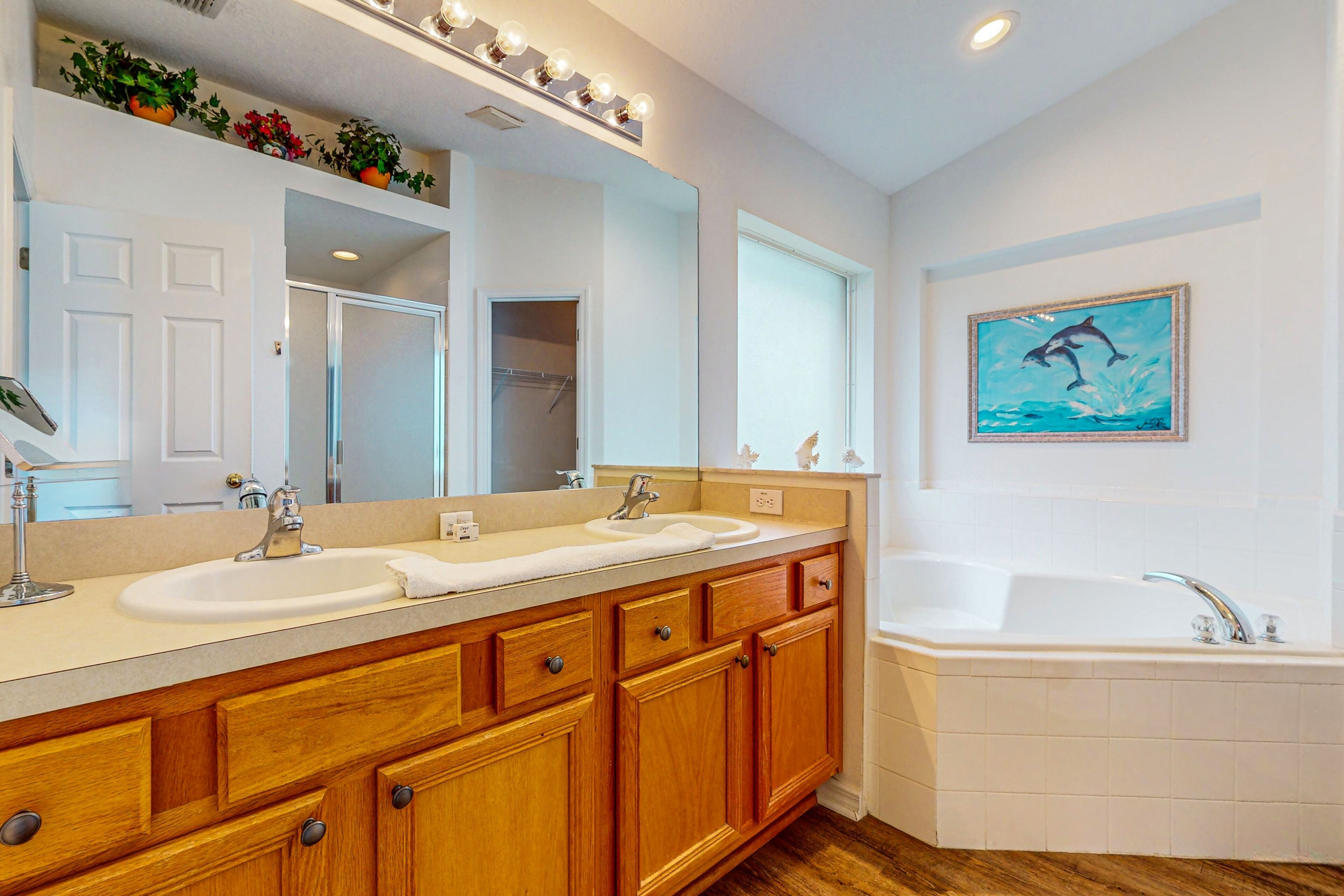 A bathroom with a double sink vanity, a bathtub, wooden cabinets, and a large mirror.