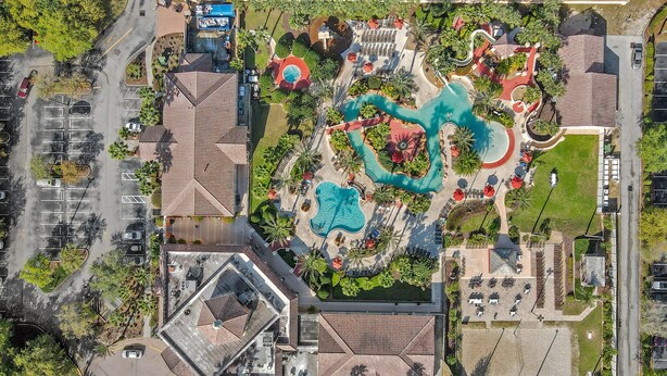Luftaufnahme eines Resorts mit mehreren Schwimmbecken, einem Parkplatz und umliegender Bepflanzung.