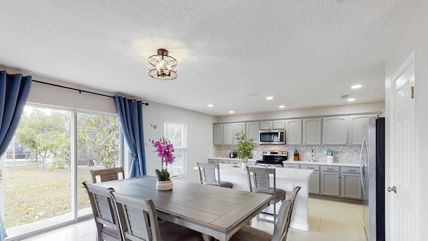 A modern kitchen with white cabinets, a central island, and a dining area with a table and chairs. - Dog-friendly Home With Lake Views, Ping-pong, air Hockey, Streaming, W/d, & AC (Kissimmee)