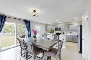 A modern kitchen with white cabinets, a central island, and a dining area with a table and chairs. - Dog-friendly Home With Lake Views, Ping-pong, air Hockey, Streaming, W/d, & AC (Kissimmee)