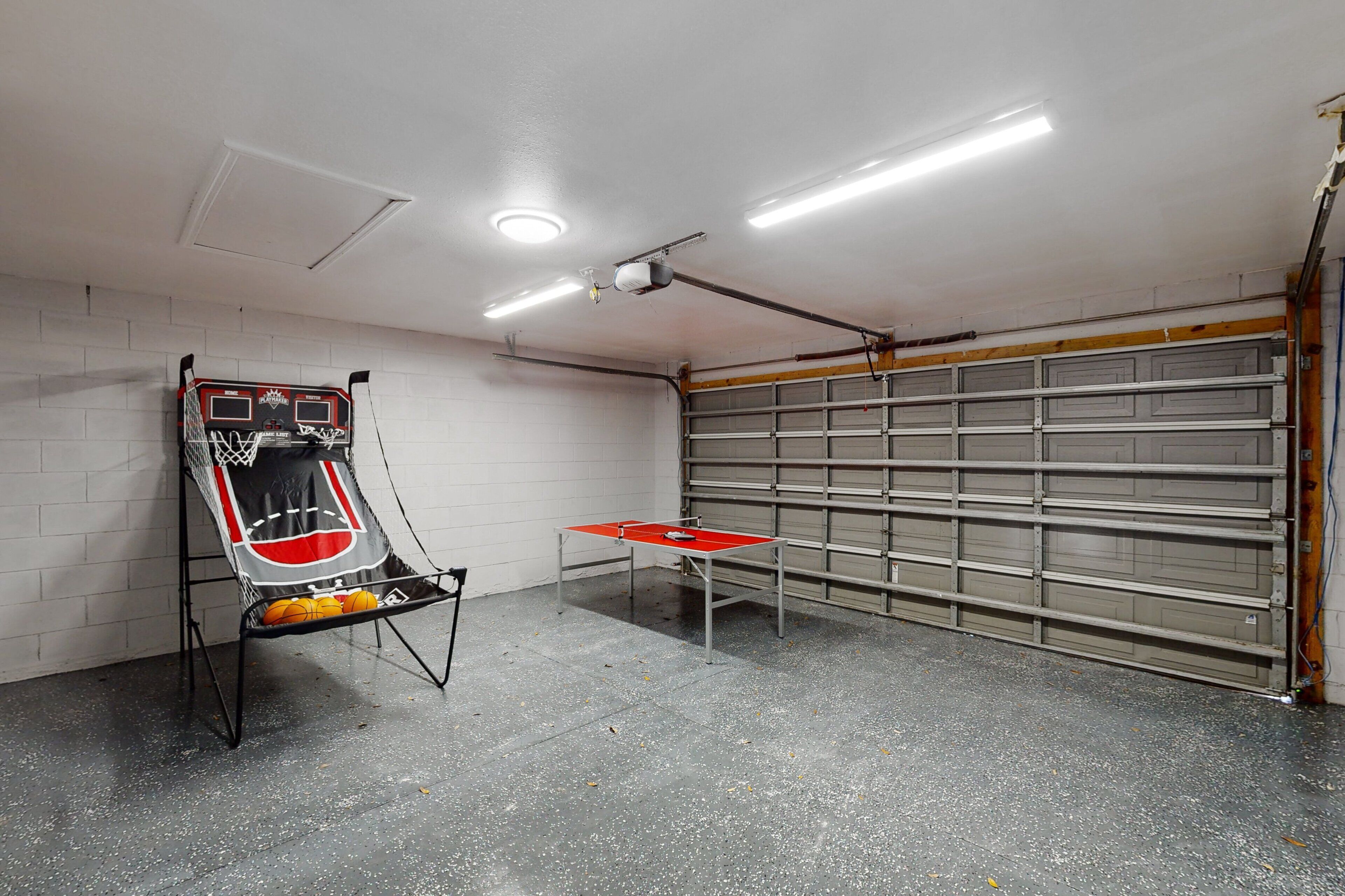 Una canasta de baloncesto, una mesa de ping pong y una puerta de garaje en un garaje.
