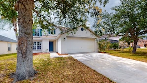 A residential house with a garage, driveway, and surrounding trees. - Dog-friendly Home With Lake Views, Ping-pong, air Hockey, Streaming, W/d, & AC (Kissimmee)