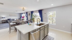 A modern kitchen with a central island, a dining area with a table and chairs, and a living room with a sofa and a coffee table. - Dog-friendly Home With Lake Views, Ping-pong, air Hockey, Streaming, W/d, & AC (Kissimmee)