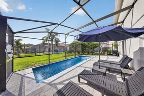 A covered outdoor swimming pool with lounge chairs and a patio umbrella. - Dog-friendly Home With Lake Views, Ping-pong, air Hockey, Streaming, W/d, & AC (Kissimmee)