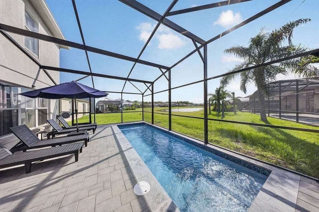 An outdoor swimming pool with lounge chairs and umbrellas, surrounded by a glass enclosure.